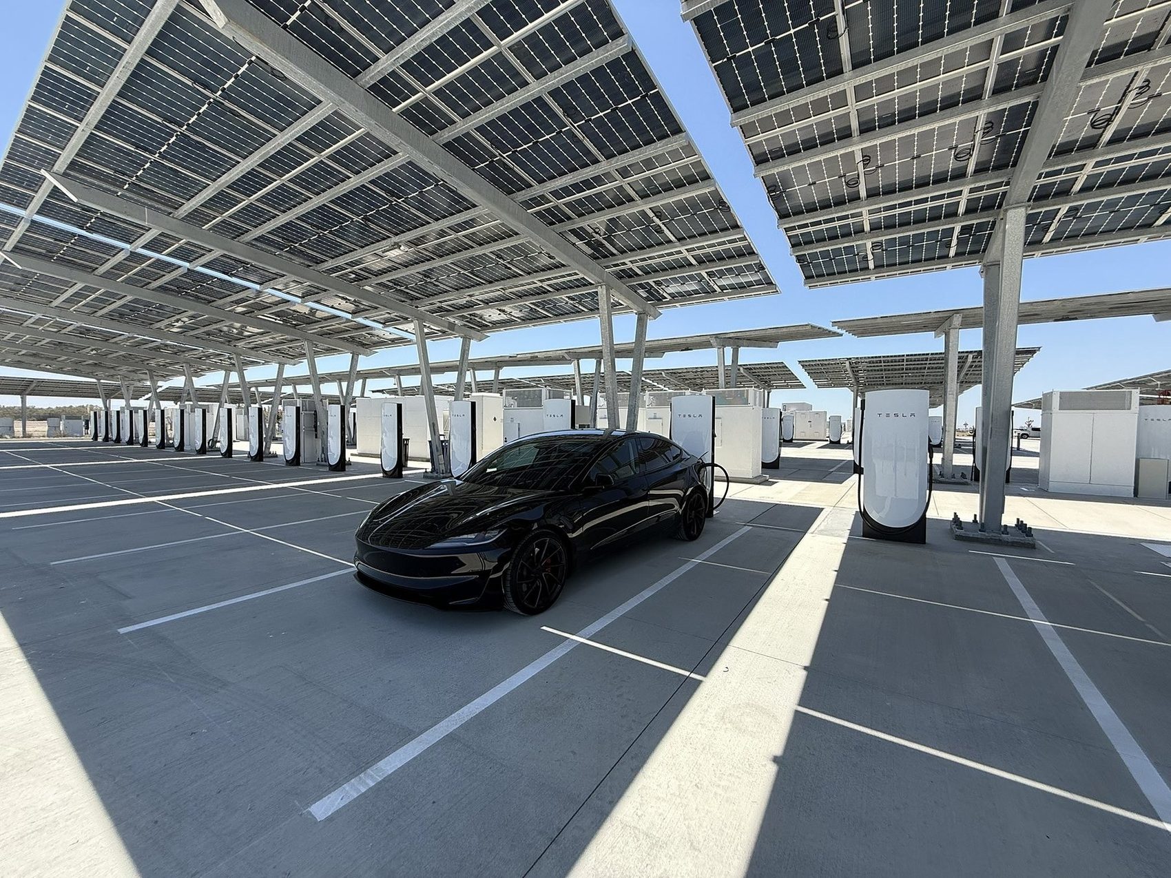 Tesla charging beneath a solar canopy at a Supercharger site